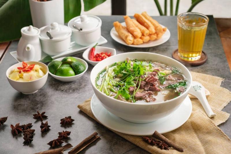 Bát lẩu cua đồng đầy đặn có cả bún, đậu phụ và riêu cua, cùng vài loại rau nhúng kèm.
