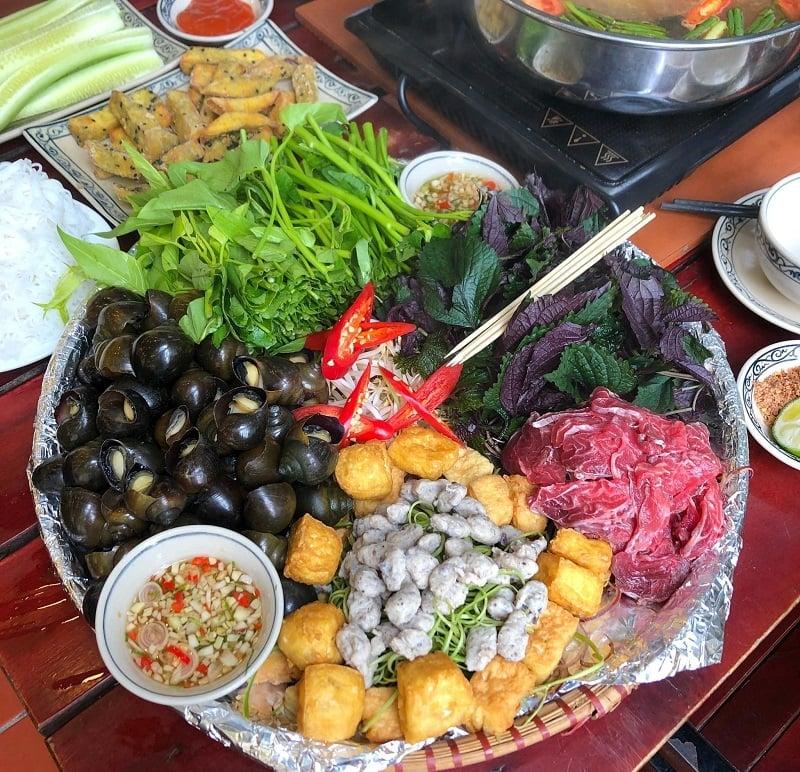 Hình ảnh một bàn ăn với nồi lẩu thái hải sản đang sôi, xung quanh bày biện các đĩa hải sản tươi, rau củ và bún, tạo không khí ấm cúng