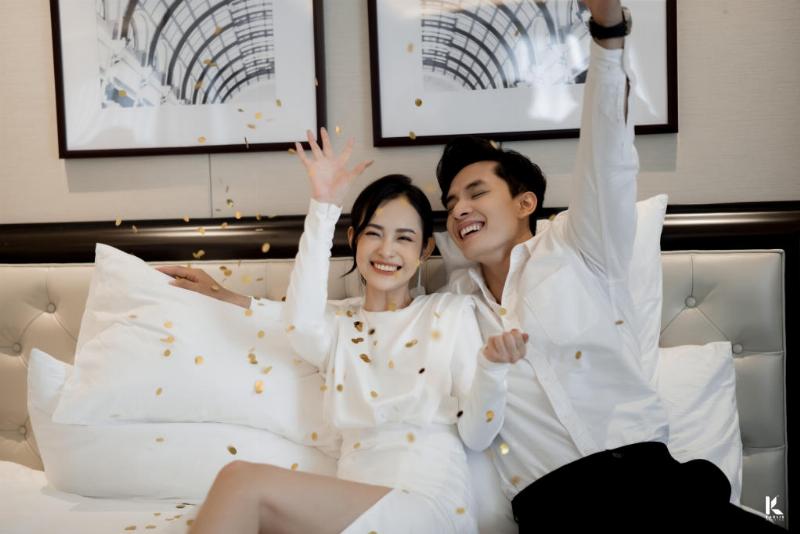 Ảnh chụp một cặp đôi cô dâu chú rể đang lắng nghe lời phát biểu chúc mừng từ một người bạn thân tại buổi tiệc cưới, biểu cảm cảm động và biết ơn.